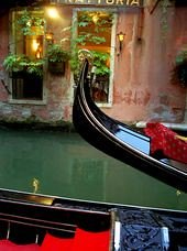 La proue d’une gondole sur un canal de Venise, devant une façade fleurie.